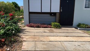 A modern building with a garage door, a concrete driveway, and a well-maintained garden with various plants and flowers. - Charming tropical beach retreat Suite 1 (Hellshire)