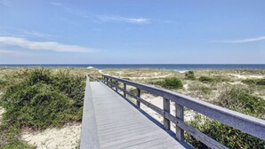 Een houten looppad dat naar een strand met duinen en schaarse begroeiing leidt.