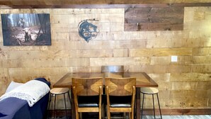 Un interior de madera con una mesa y sillas, un cartel de bienvenida enmarcado y un cuadro en la pared.