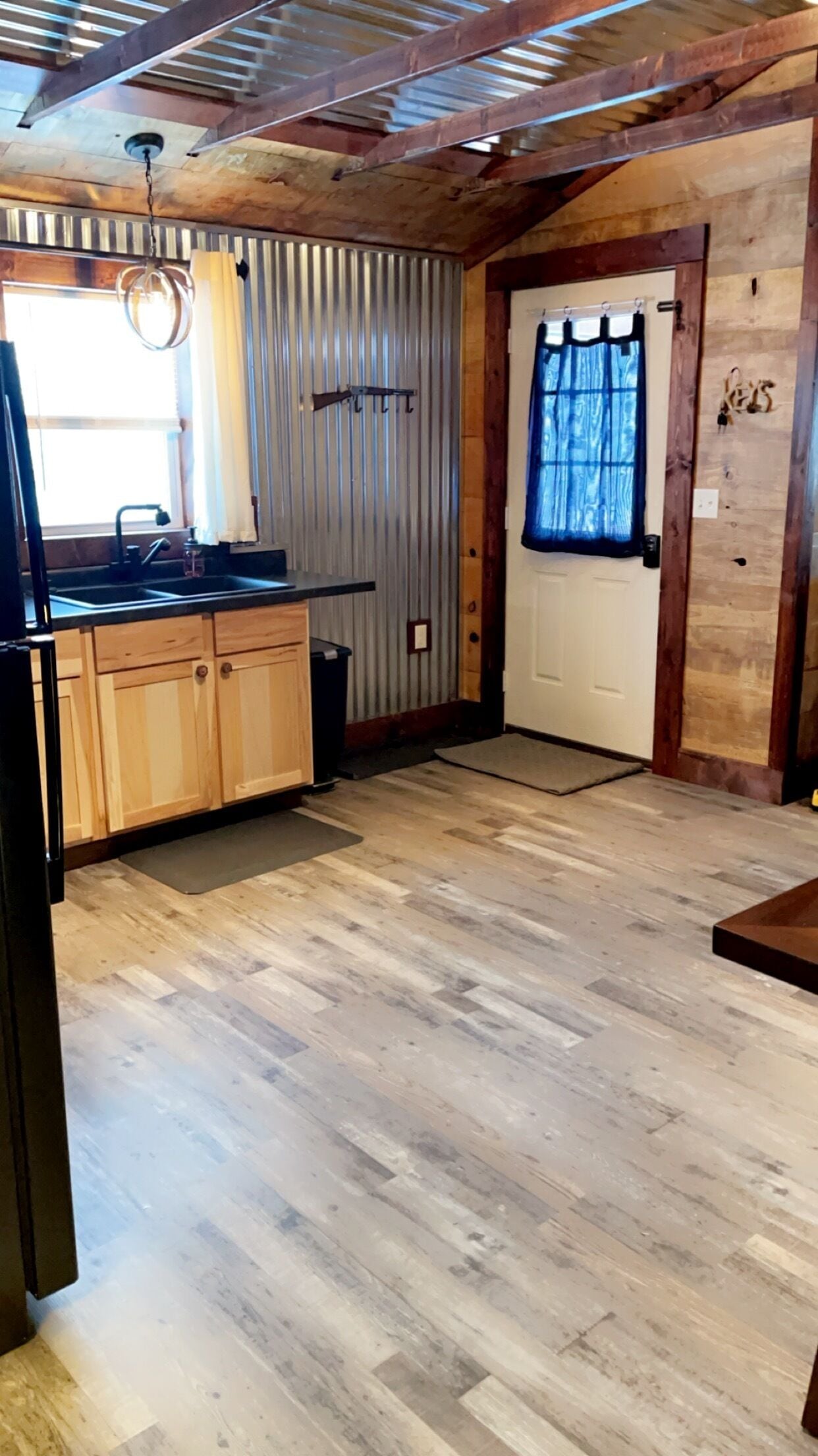 A compact kitchen with wooden cabinets, a black countertop, and a window with curtains.
