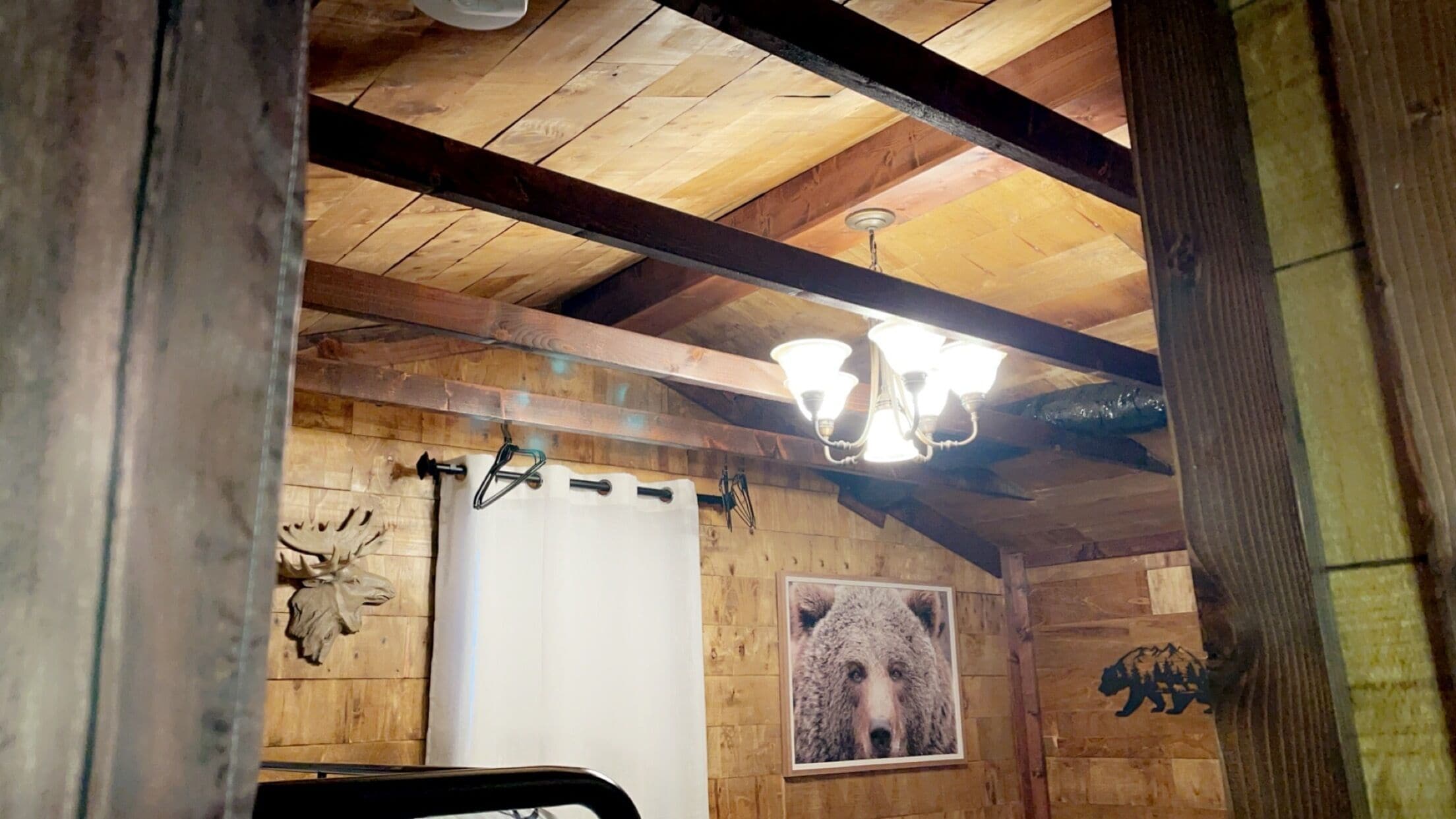 L’intérieur d’un chalet en bois, avec des poutres apparentes, un lustre, un tableau représentant un ours et une décoration en forme de tête d’ours.