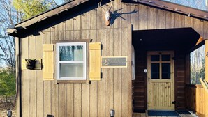 Una cabaña de madera con puerta principal, ventana y letrero de madera.