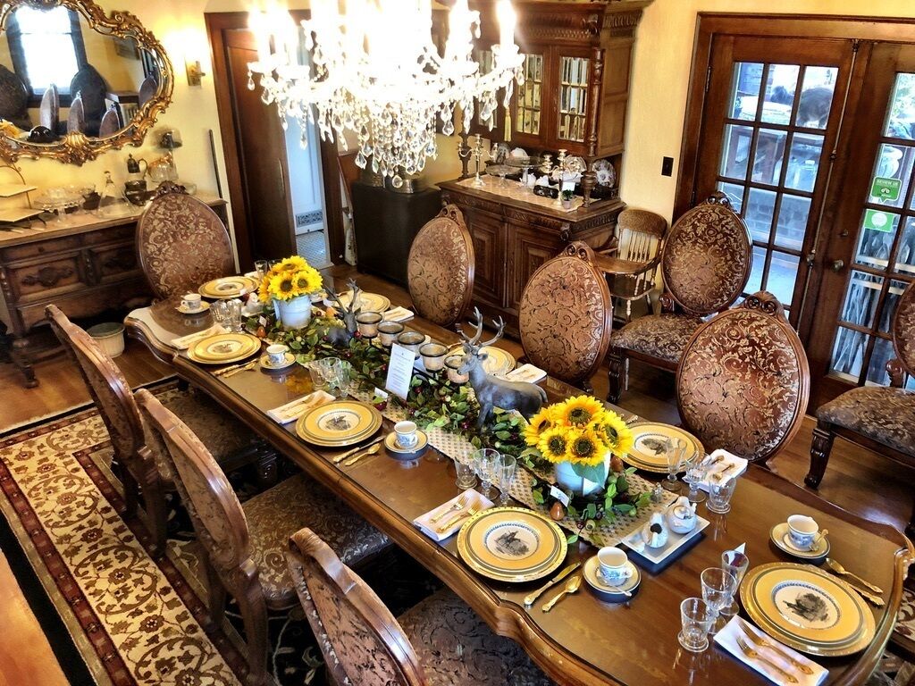 Un comedor formal con una larga mesa dispuesta para una comida, rodeada de sillas ornamentadas.