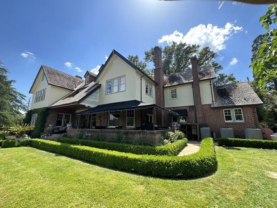 A two-story house with a covered patio, brick exterior, and a well-maintained lawn.