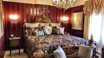 A luxurious bedroom with a large ornate bed, two wall sconces, a chandelier, and a framed picture on the wall.