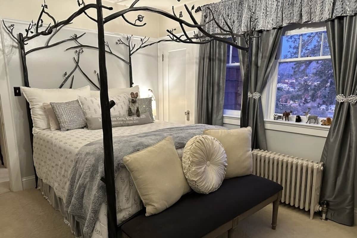 A bedroom with a four-poster bed, a bench, and a window with curtains.