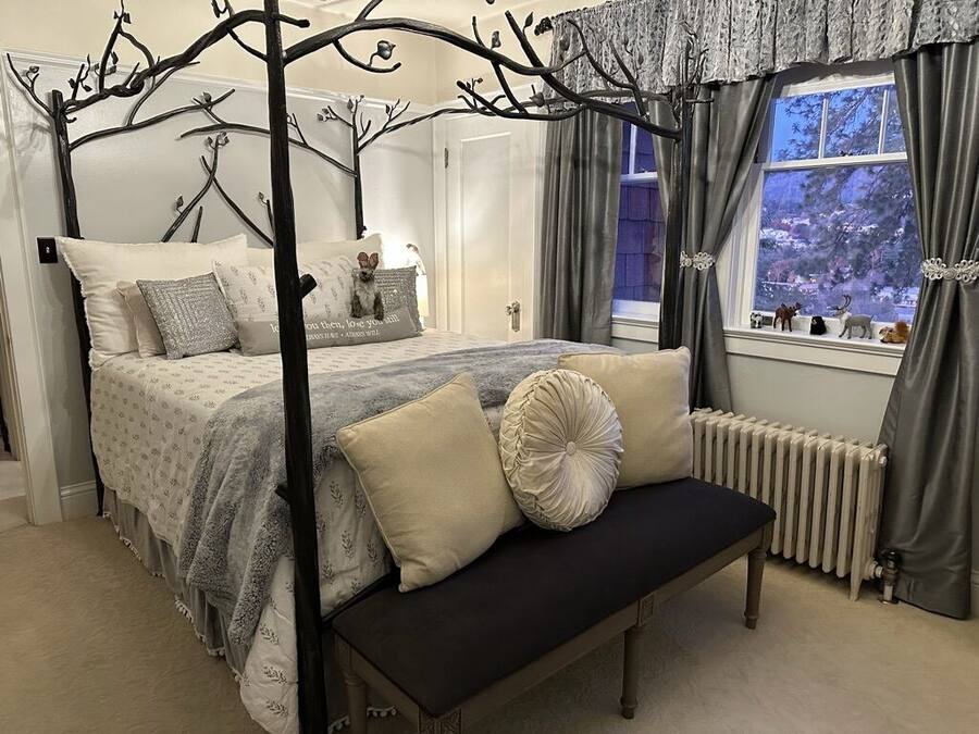A bedroom with a four-poster bed, a bench, and a window with curtains.