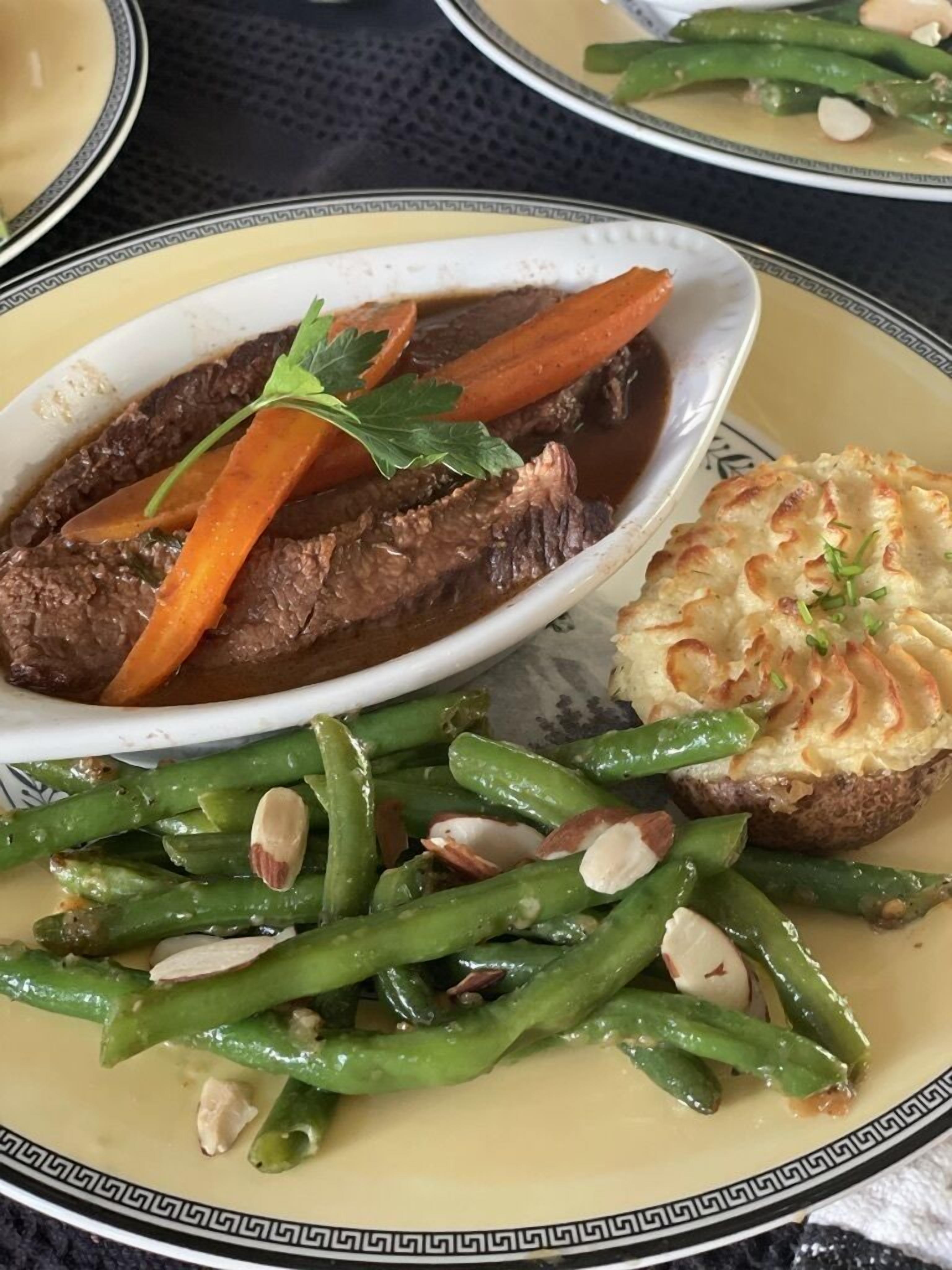 A plate with beef, carrots, green beans, and a baked potato.
