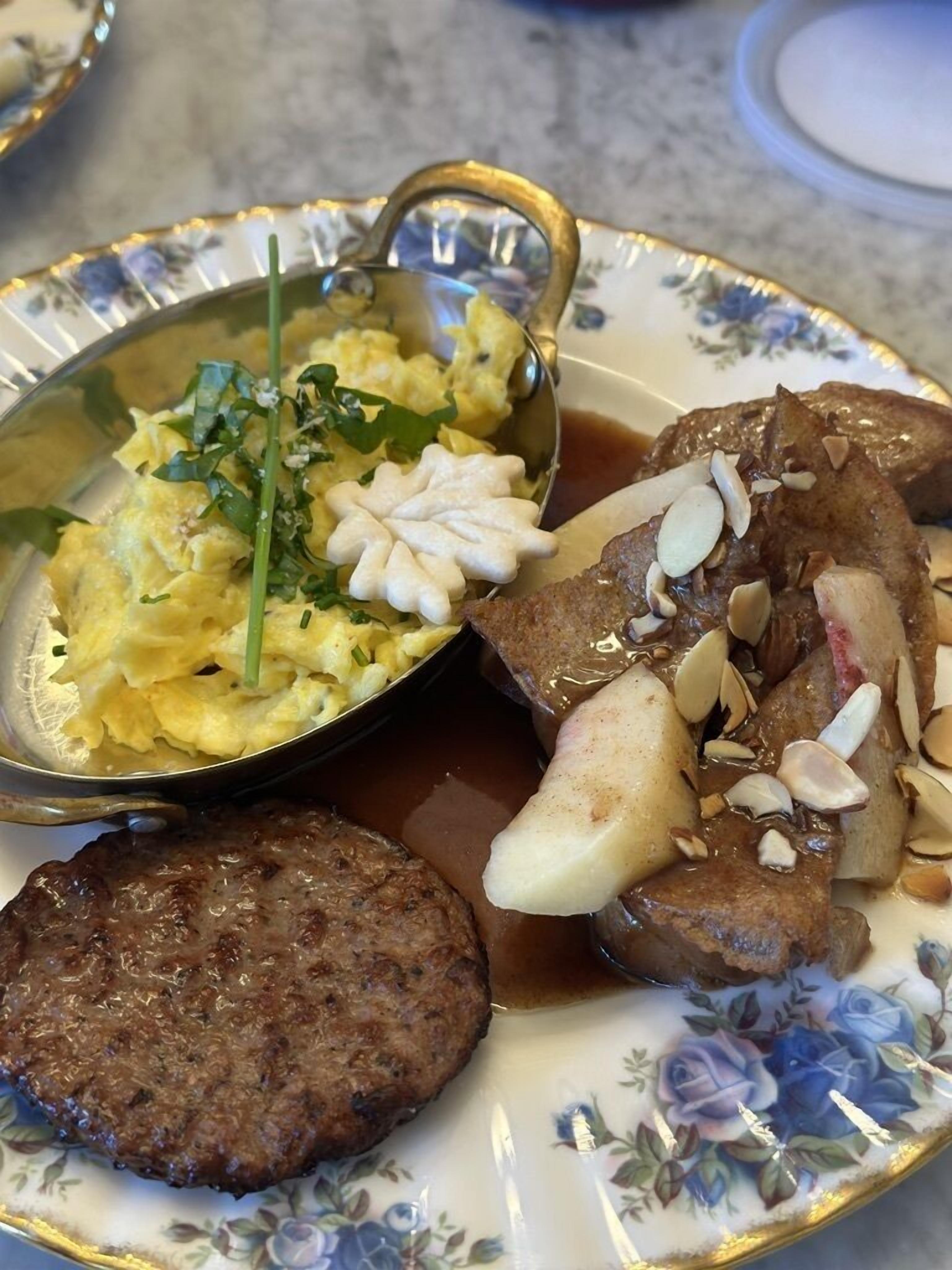 A plate with scrambled eggs, a meat patty, and a side of potatoes with almonds.