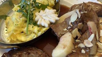 A plate with scrambled eggs, a meat patty, and a side of potatoes with almonds.