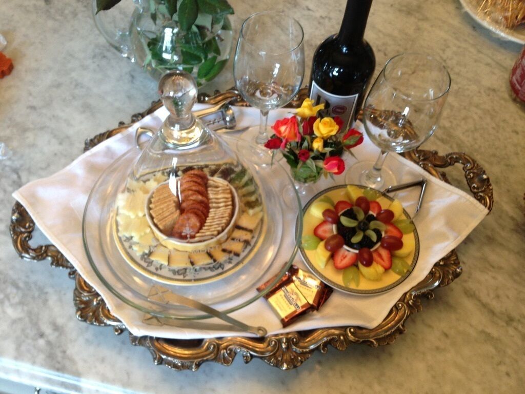 Une table avec un présentoir à gâteaux en verre, un saladier de fruits, une bouteille de vin et une petite boîte de chocolats.