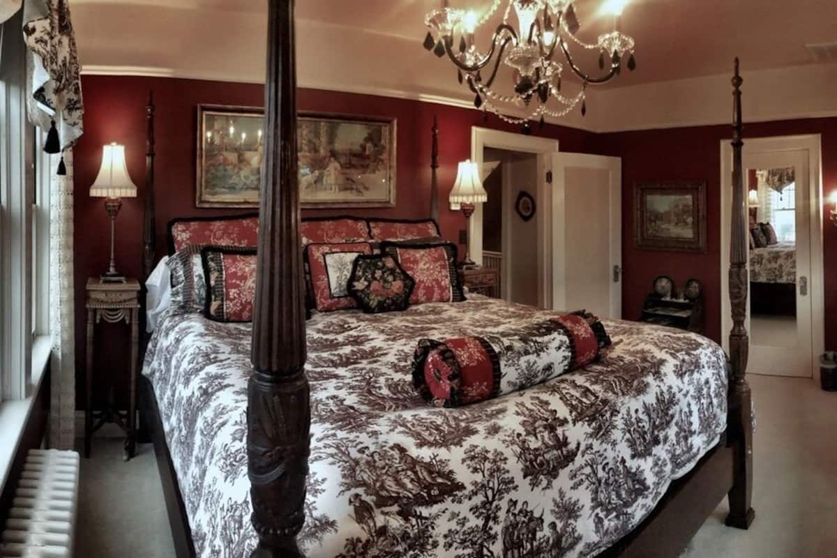 A bedroom with a four-poster bed, a chandelier, and a mirror.