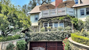 Une voiture ancienne est garée devant une grande maison dotée d’un balcon et d’un garage.