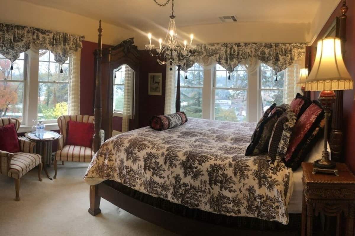 A bedroom with a large bed, a chair, a small table, and a chandelier.