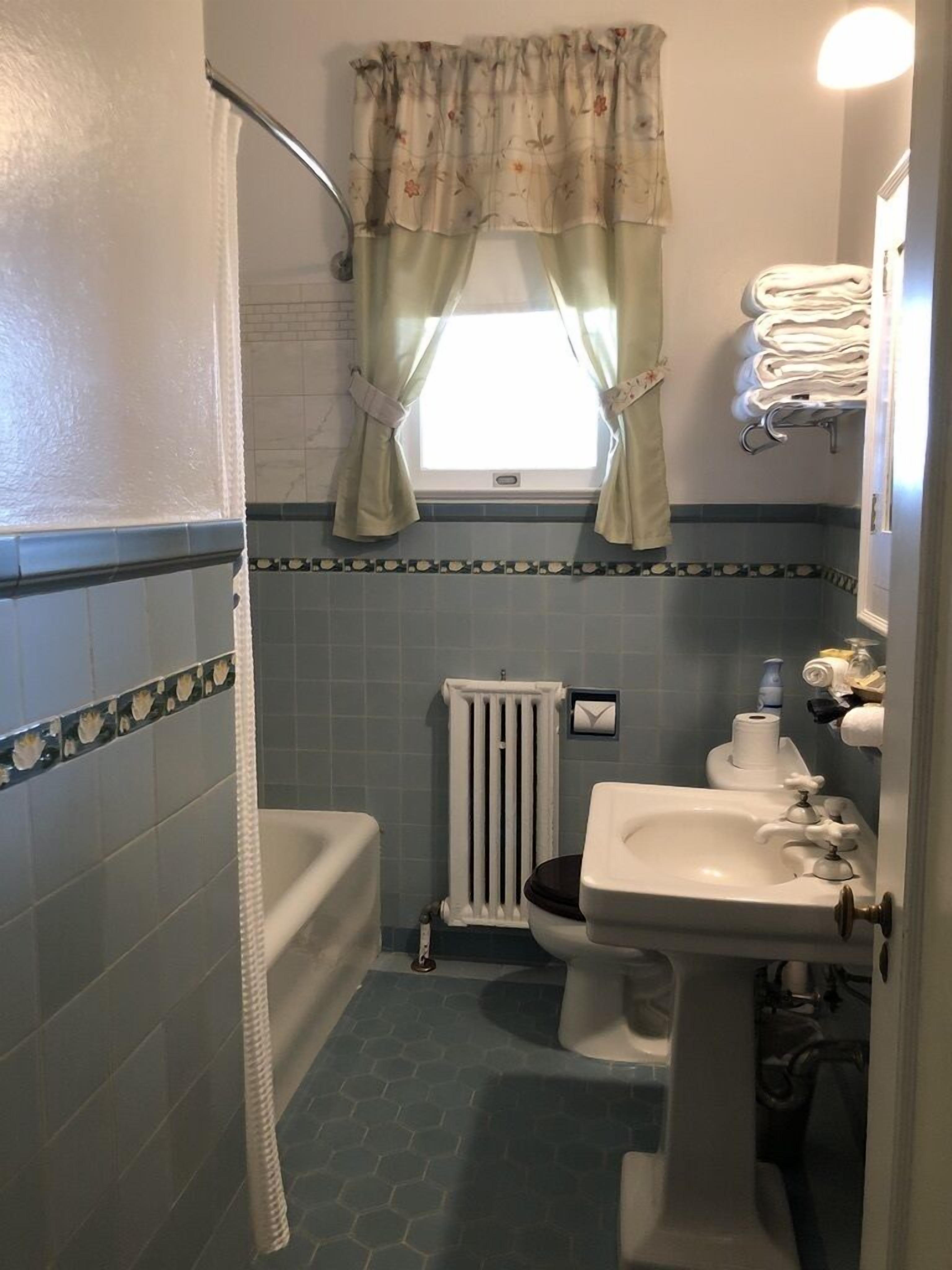 Un baño con bañera, inodoro, lavabo y ventana con cortinas.