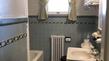 Un baño con bañera, inodoro, lavabo y ventana con cortinas.