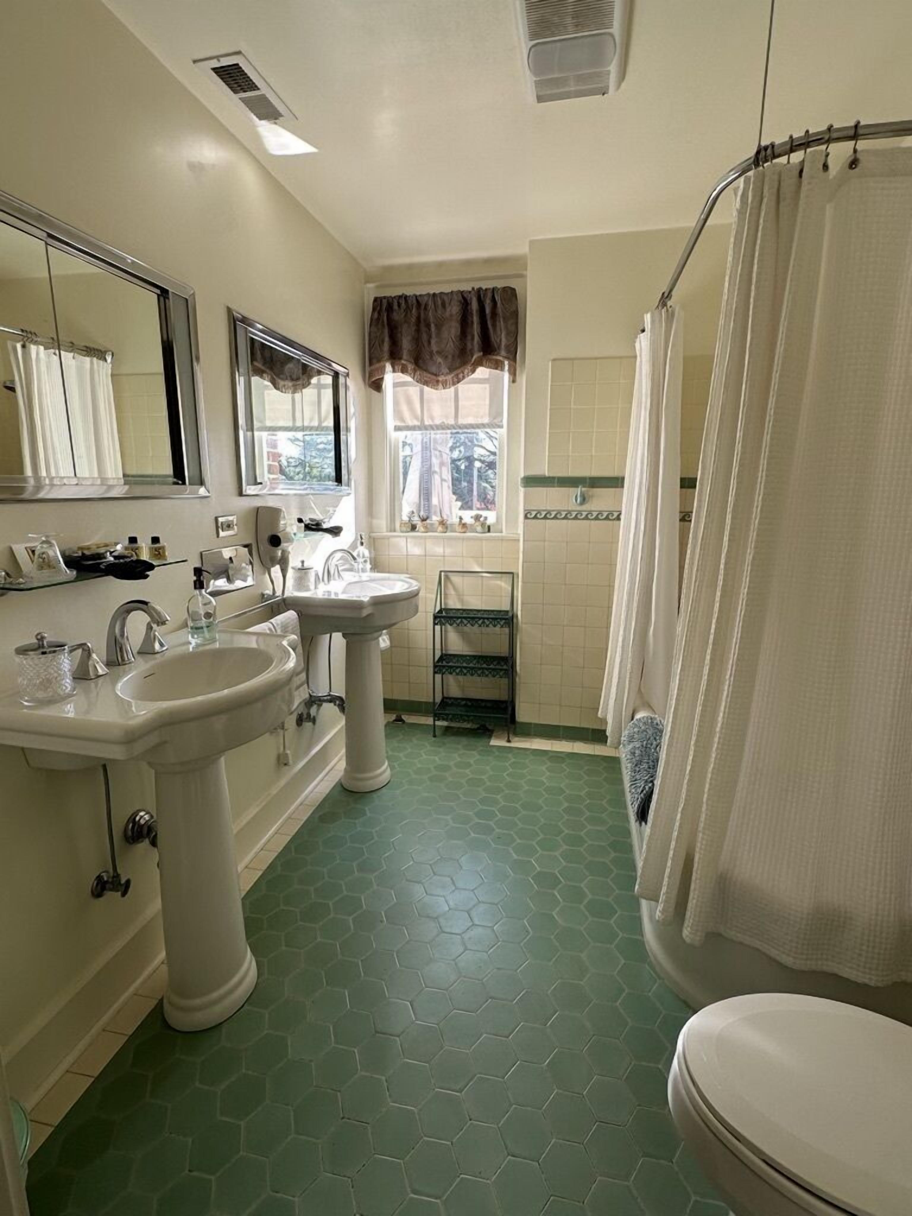 Une salle de bain avec deux lavabos, des toilettes, une douche avec un rideau et une fenêtre également dotée de rideaux.