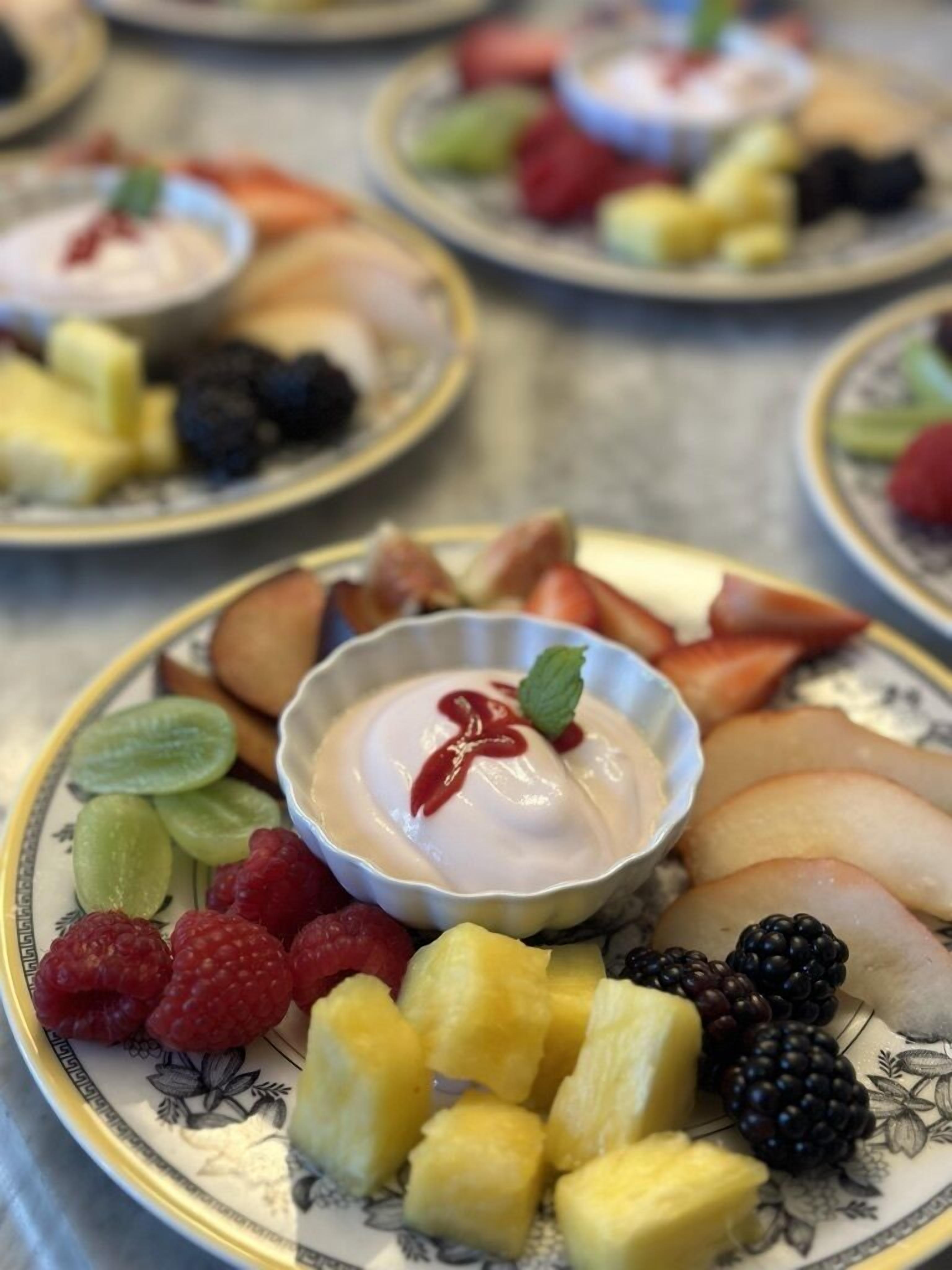 Una bandeja de postres con diversas frutas y un tazón pequeño de yogur.