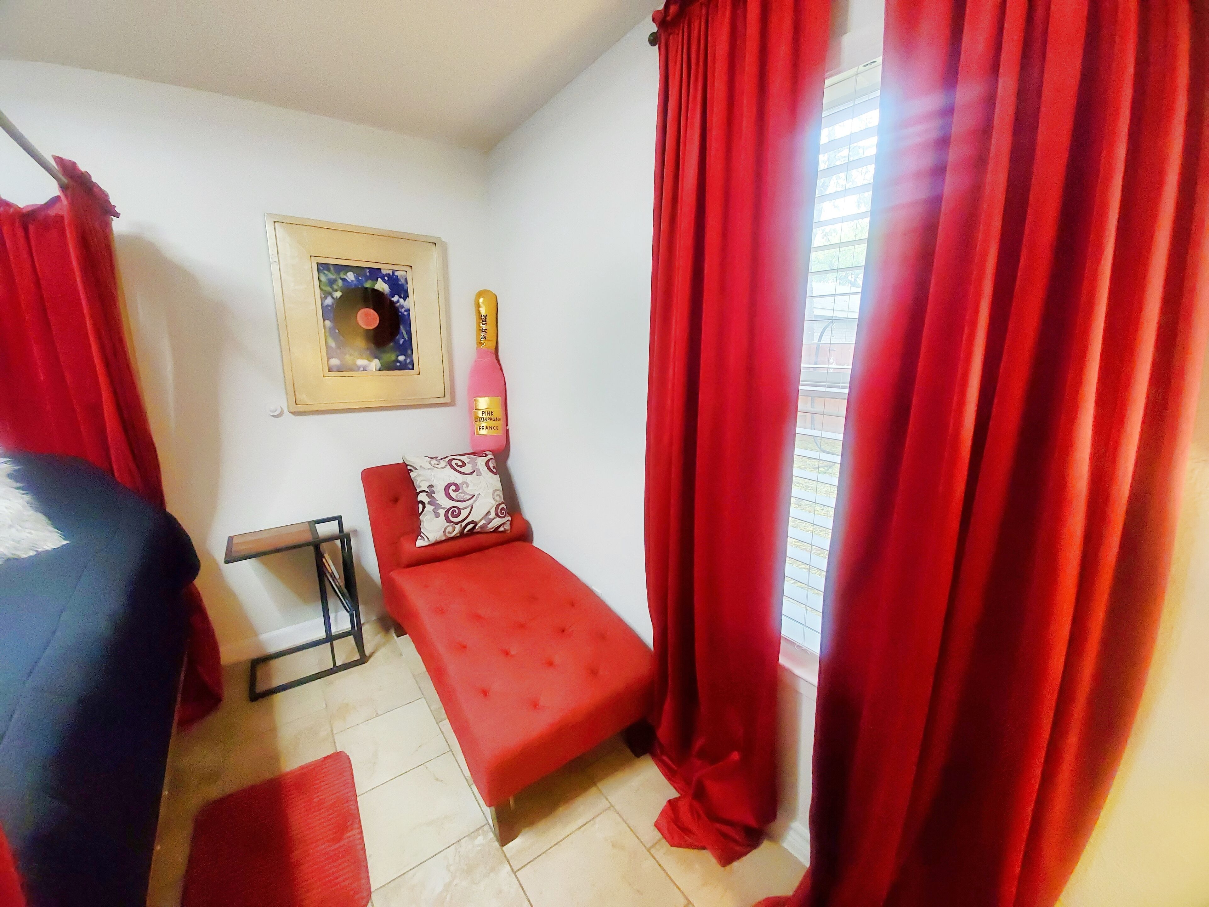 Una habitación pequeña con una cama roja, una silla roja, una mesita y una ventana con cortinas rojas.