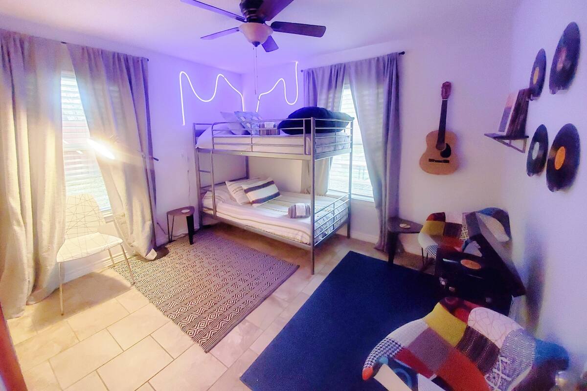 A room with bunk beds, a ceiling fan, a guitar, and wall decorations.
