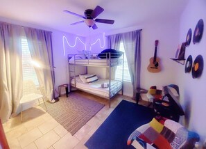 Een kamer met stapelbedden, een plafondventilator, een gitaar en wanddecoraties.