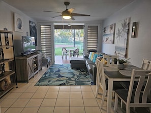 Relax in this spacious living area with a sofa, dining table, and kitchenette, offering a garden view.