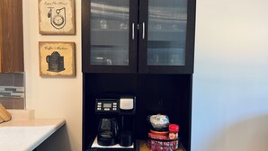 Une cuisine équipée d’une machine à café, d’un meuble avec des portes en verre et d’œuvres d’art décoratives au mur.