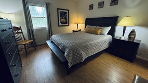 Une chambre à coucher comprenant un lit, une commode en bois, une chaise, des tables de chevet et des œuvres d’art murales.