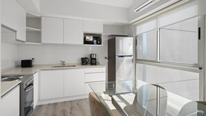 Una cocina moderna con armarios blancos, una mesa de comedor de cristal y un horno empotrado.