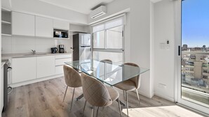 Una cocina moderna con armarios blancos, una mesa de comedor de vidrio y vistas a la ciudad a través de un ventanal grande.