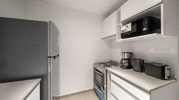 A compact kitchen with a refrigerator, stove, microwave, coffee maker, and toaster.