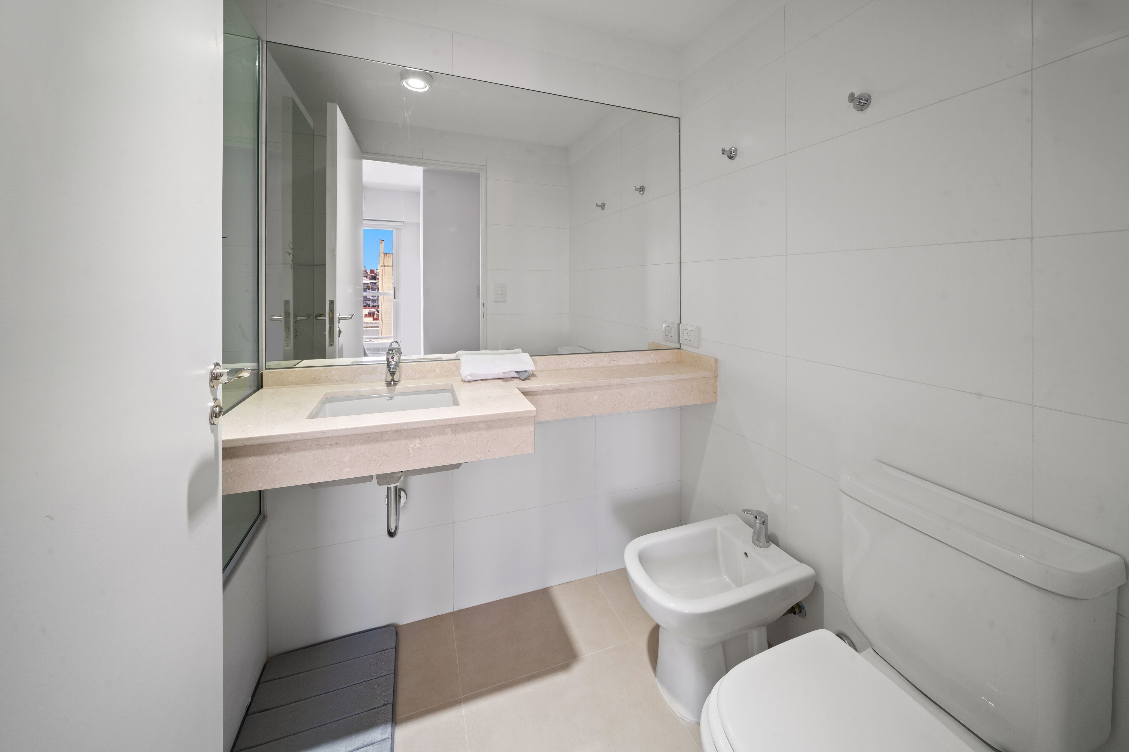 A modern bathroom with a large mirror, a sink, a bidet, and a toilet.