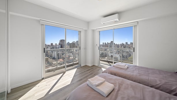 Un dormitorio moderno con dos camas, ventanas amplias y vistas a la ciudad.