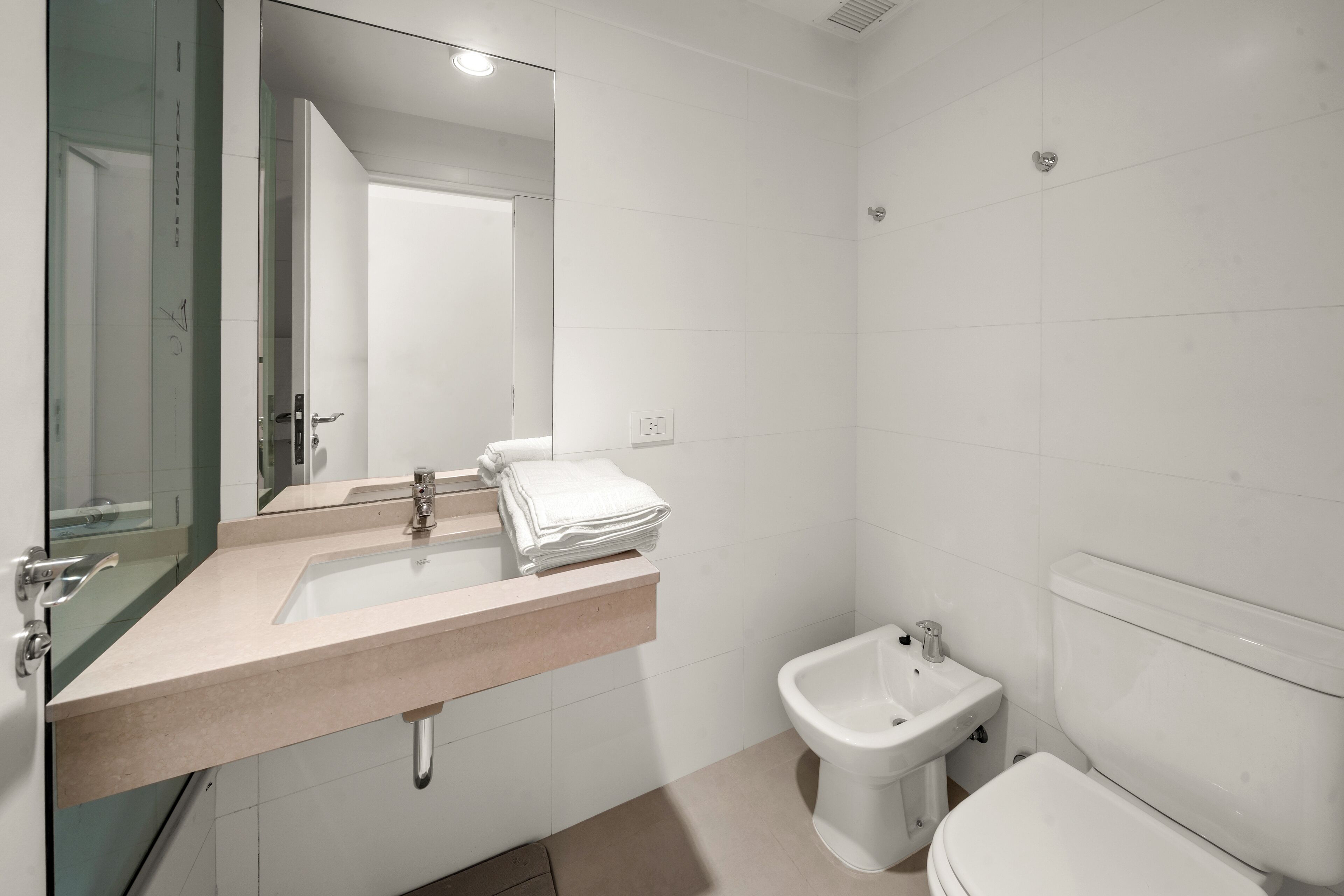 Un baño moderno con lavamanos, espejo, inodoro y bidé.