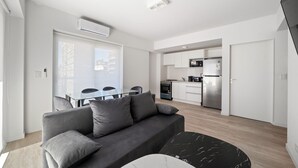 Un apartamento moderno con un sofá gris, una mesa de comedor y una zona de cocina.