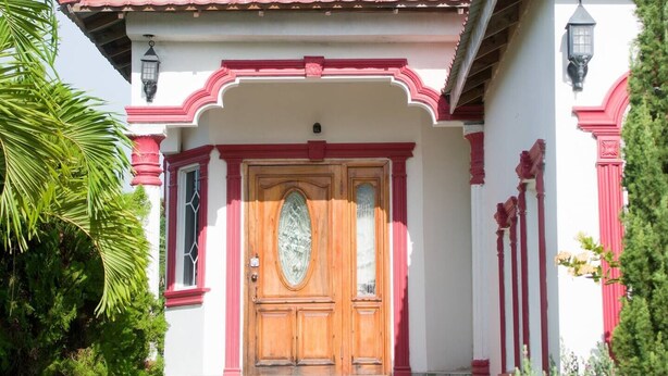 Un edificio con una puerta de madera destacada, un acceso con azulejos y una fachada roja y blanca.