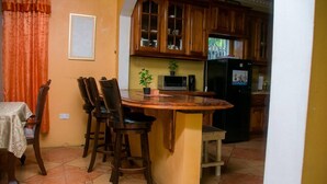 Una cocina con armarios de madera, una isla central con taburetes altos, un refrigerador y un microondas.