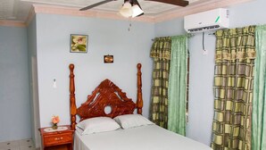 Un dormitorio con cama de madera, mesita de noche, aire acondicionado instalado en la pared y ventana con cortinas verdes.
