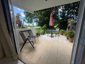 A patio area with a table and chairs, surrounded by potted plants and a view of a green landscape.