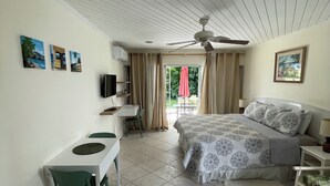Un dormitorio con cama, escritorio y silla. Hay un ventilador de techo, una ventana con cortinas y un cuadro en la pared.