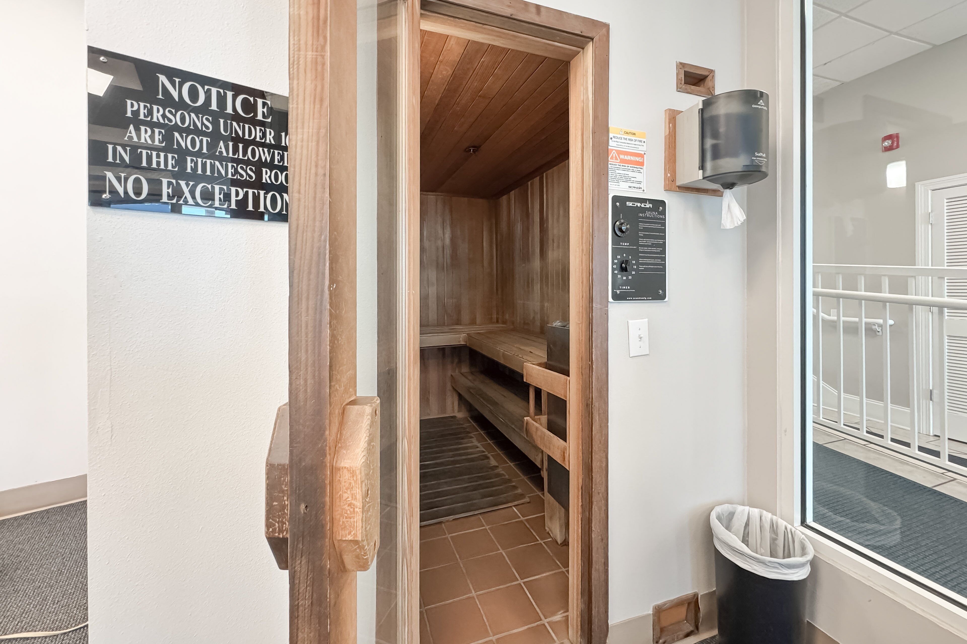 A fitness room with a wooden bench, a towel dispenser, and a notice sign.