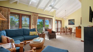 A spacious living room with a blue sofa, a wooden coffee table, and a dining area with wooden chairs and a table. - Kahala 433 | Ocean View 1BR at Poipu Kai, Walk to Beach (Koloa)