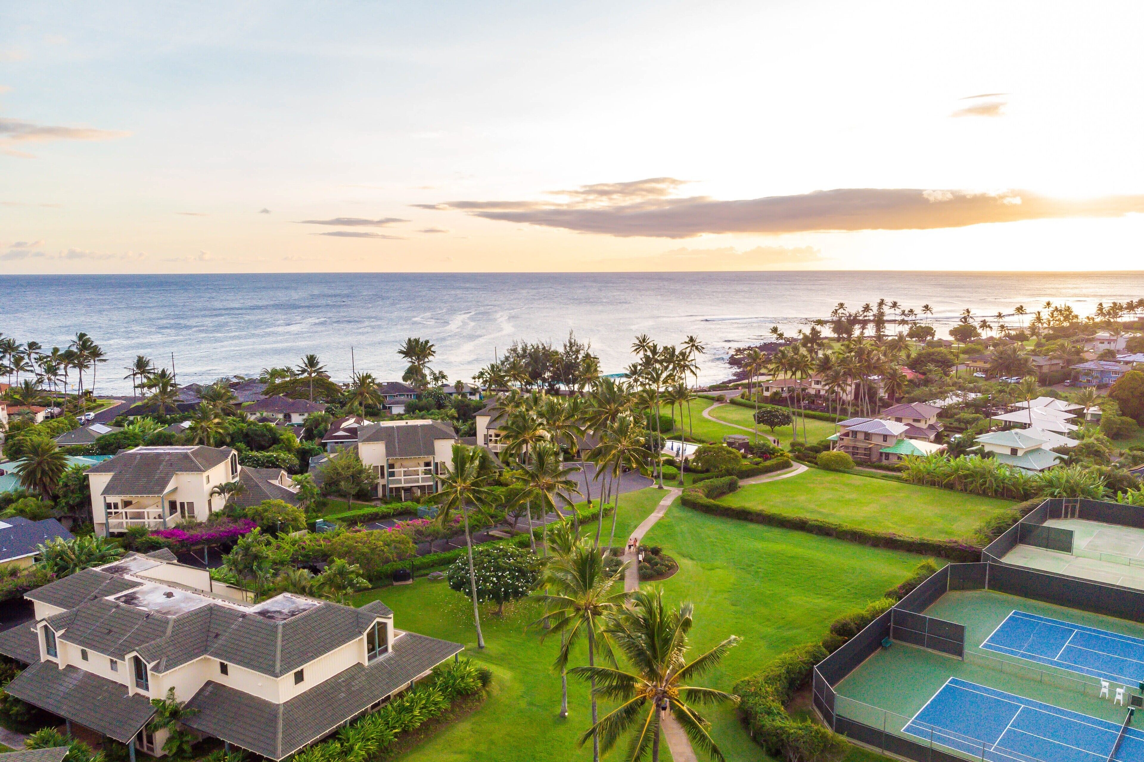 A residential area with houses, a tennis court, and a view of the ocean.