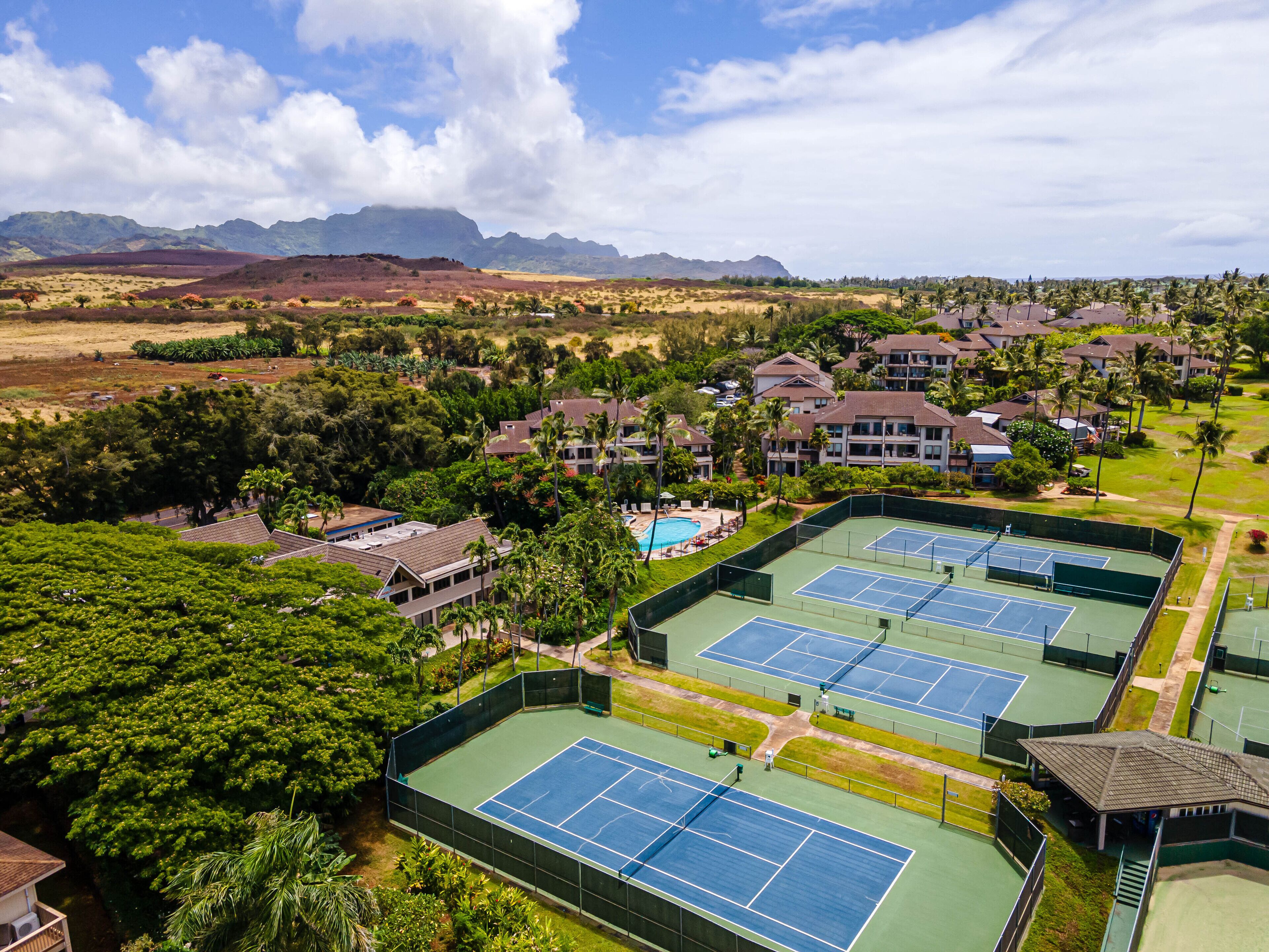 Un resort con varias canchas de tenis, una piscina y vistas a la montaña.