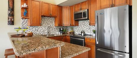 A kitchen with wooden cabinets, a stainless steel refrigerator, and a granite countertop.