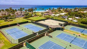 Un complex de pistes de tennis amb diverses pistes, envoltat de vegetació exuberant i vistes a l'oceà.