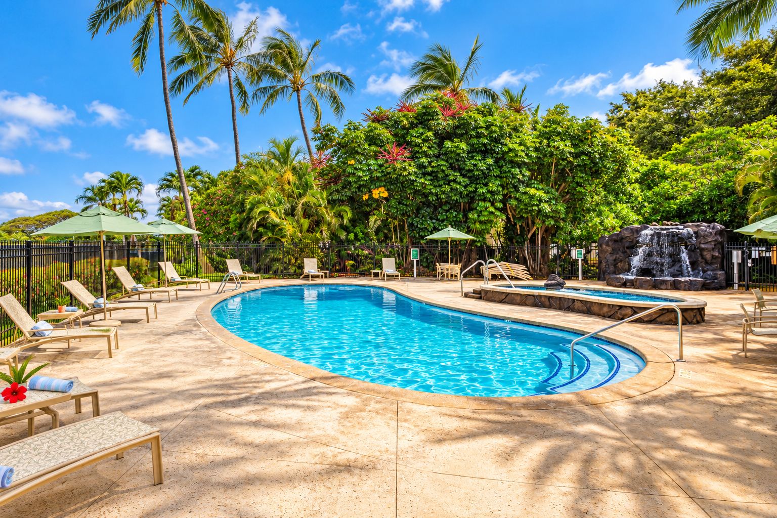 A pool area with lounge chairs, a small waterfall feature, and lush tropical vegetation.
