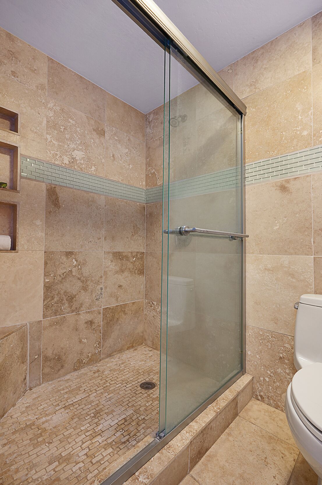A glass-enclosed shower with beige tiles and a glass door.