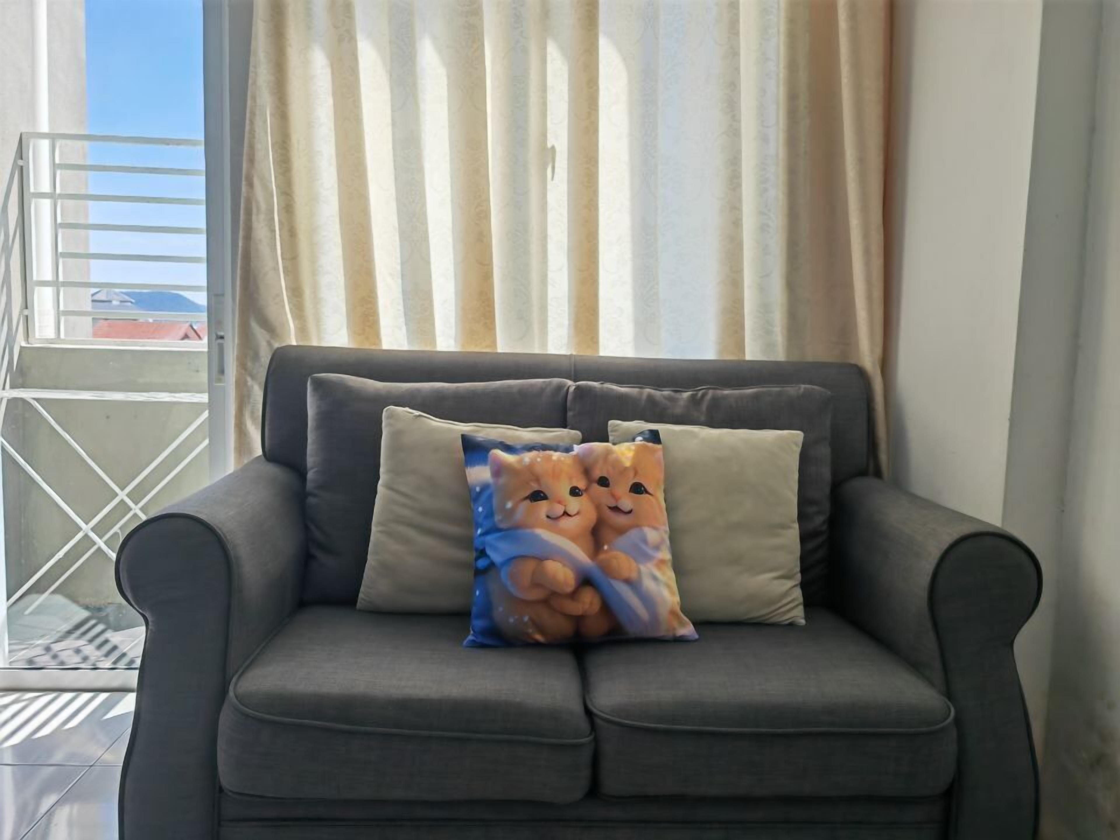A grey sofa with two cushions, one featuring a cat design.