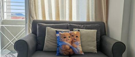 A grey sofa with two cushions, one featuring a cat design.
